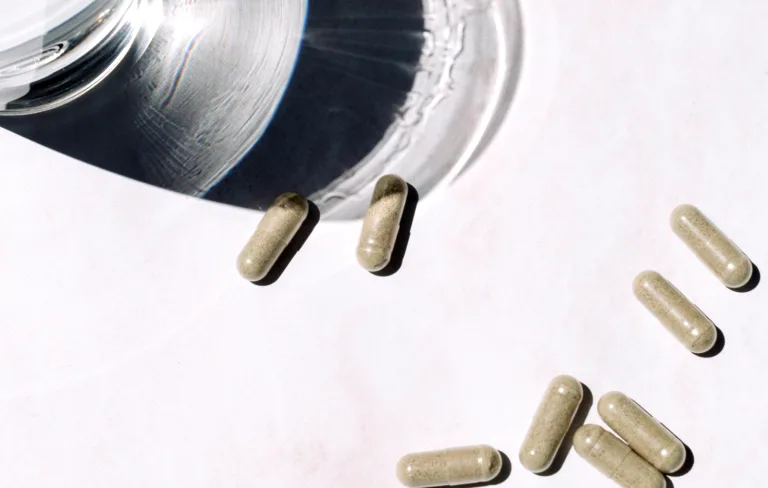 Assorted sakara.momplete Probiotic Formula capsules scattered on a light surface beside a glass container.