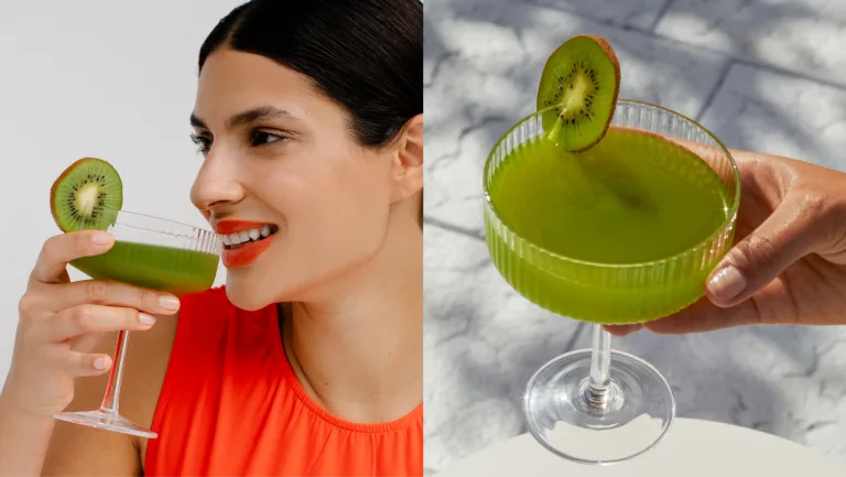 Woman holding a green cocktail in a stemmed glass garnished with a kiwi slice.