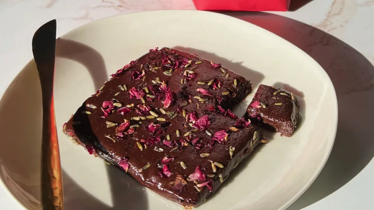 Chocolate-glazed truffle bars square topped with dried rose petals on a cream-colored plate.