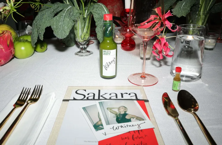 Overhead shot of a dining table with fresh produce, Tabasco sauce, a martini, and Sakara menu.