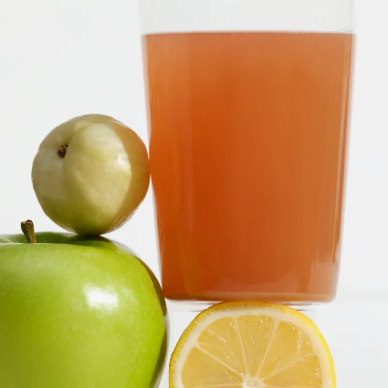 Glass of water mixed with Sakara Fiber Super Powder beside green apple and sliced lemon on white background