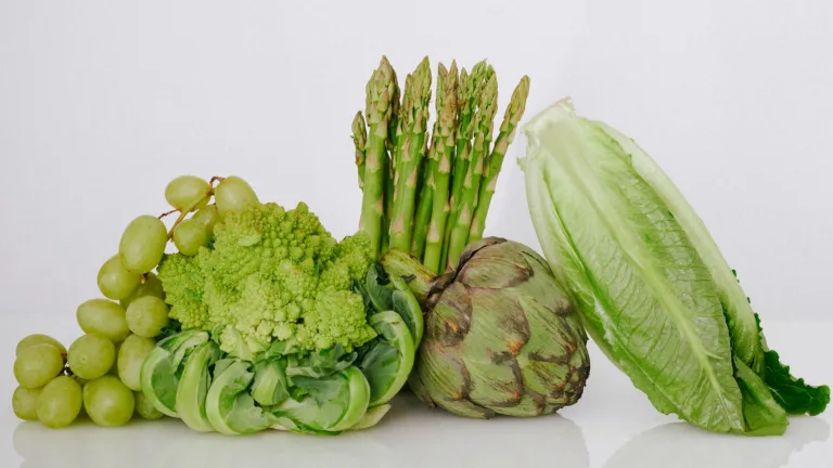 Assorted fresh produce including asparagus, romaine lettuce, green grapes, cauliflower, and an artichoke.