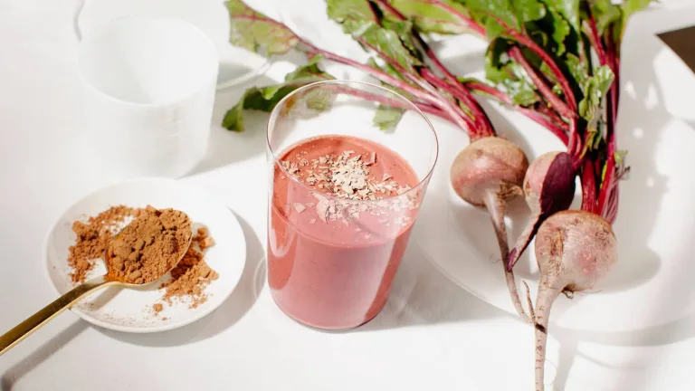 Red Velvet Metabolism Smoothie in a glass beside fresh beets and a small dish of Sakara Metabolism Super Powder.