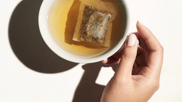 Cup of tea with a tea bag resting inside, held by a hand.