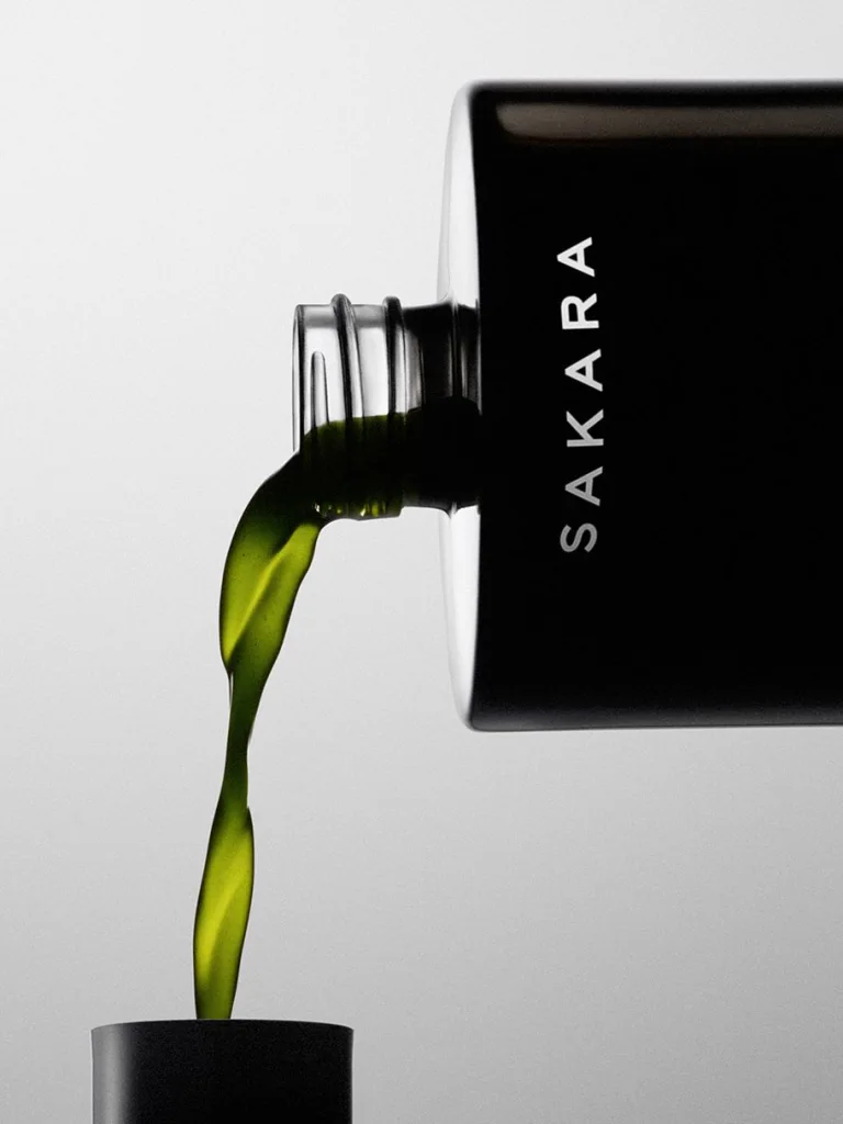 Green Daily Elixir liquid multivitamin being poured from a Sakara bottle into a cap, showing the green liquid.