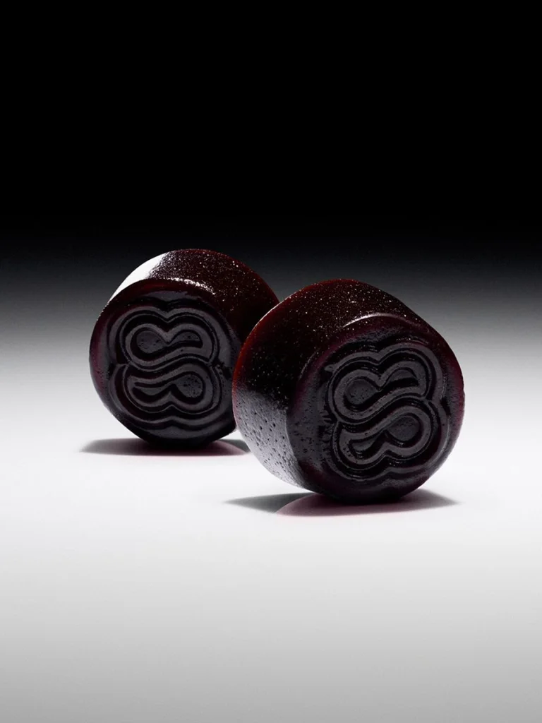 Two dark red Sakara Metabolism Bite thermogenic gummies with embossed logo on gradient gray-to-black background