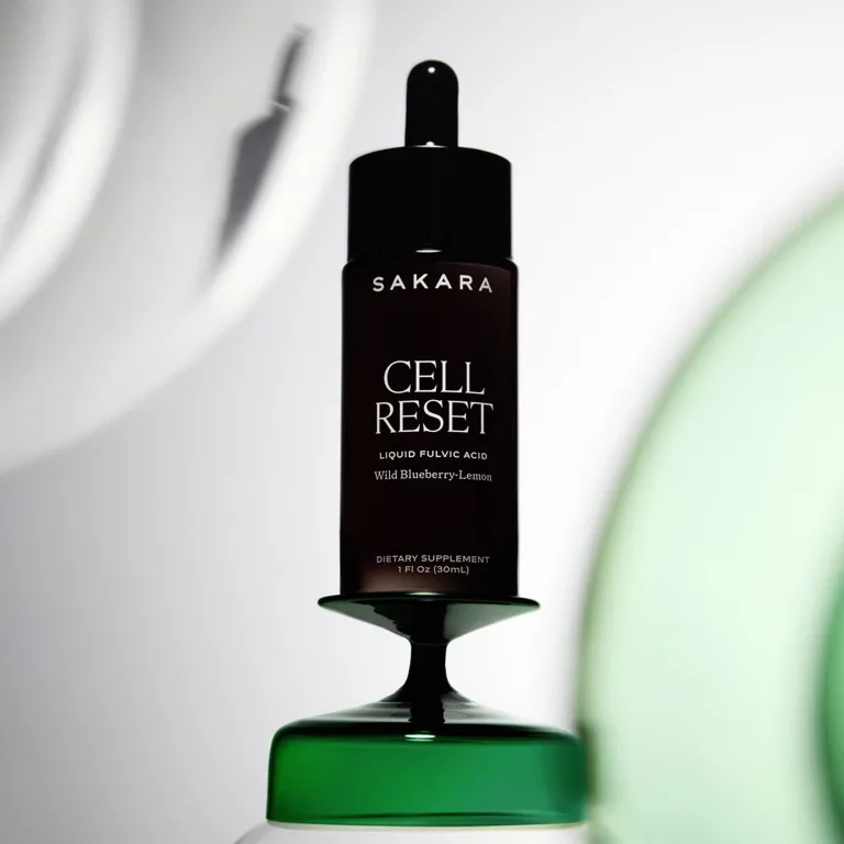 Sakara Cell Reset liquid fulvic acid in dark glass dropper bottle with black cap, wild blueberry-lemon flavor, 1 fl oz (30 mL), shown styled on green pedestal.