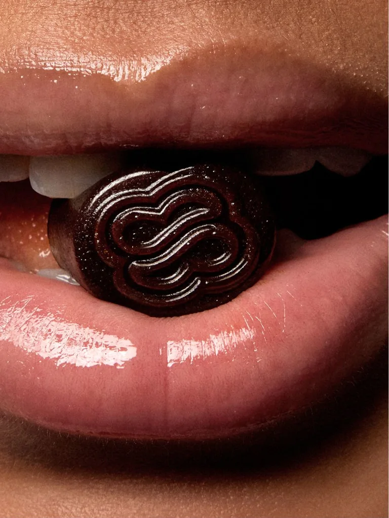 Sakara Life purple metabolism bite gummy with logo engraved in it; model's mouth with gummy touching lips