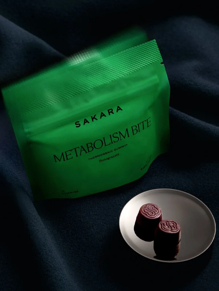 Sakara Metabolism Bite thermogenic gummies in bright green resealable pouch with black text, pomegranate flavor, 14 gummies dietary supplement, shown with two dark red gummies on white plate