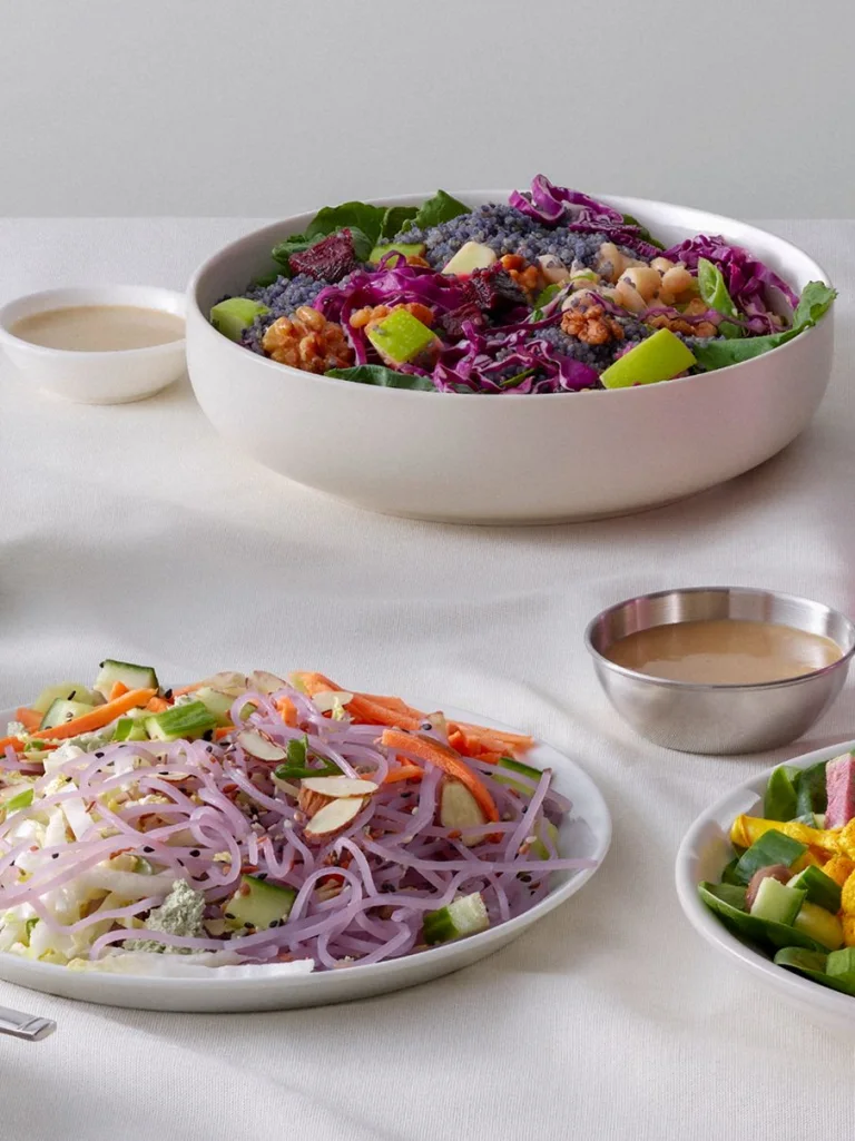 Sakara Level II: Detox plant-based meals arranged on a white table including mixed salads, soup, and dressing in small bowls.