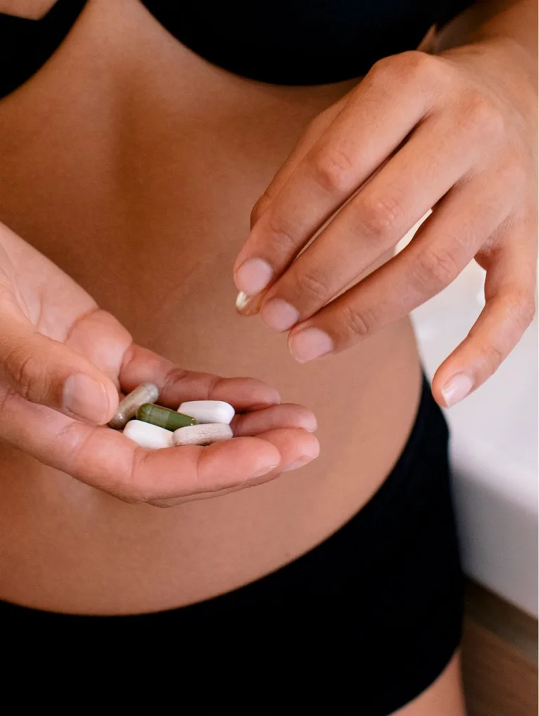 Sakara The Foundation: Prenatal capsules held in a pregnant female's hand in soft indoor lighting.