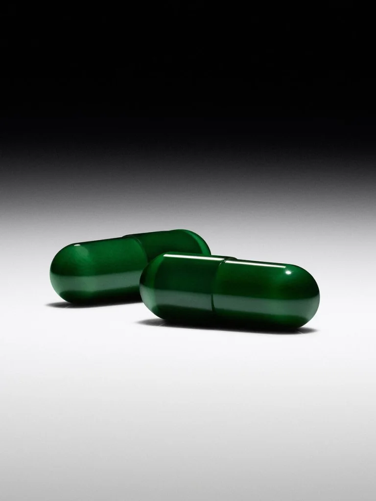 Two glossy green Sakara Beauty Biome capsules on faded background