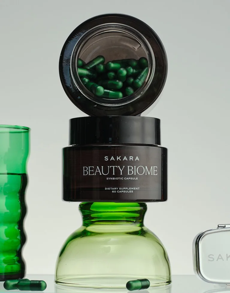 Sakara Beauty Biome packaging stacked on top of a green cup; green capsules in black glass jar