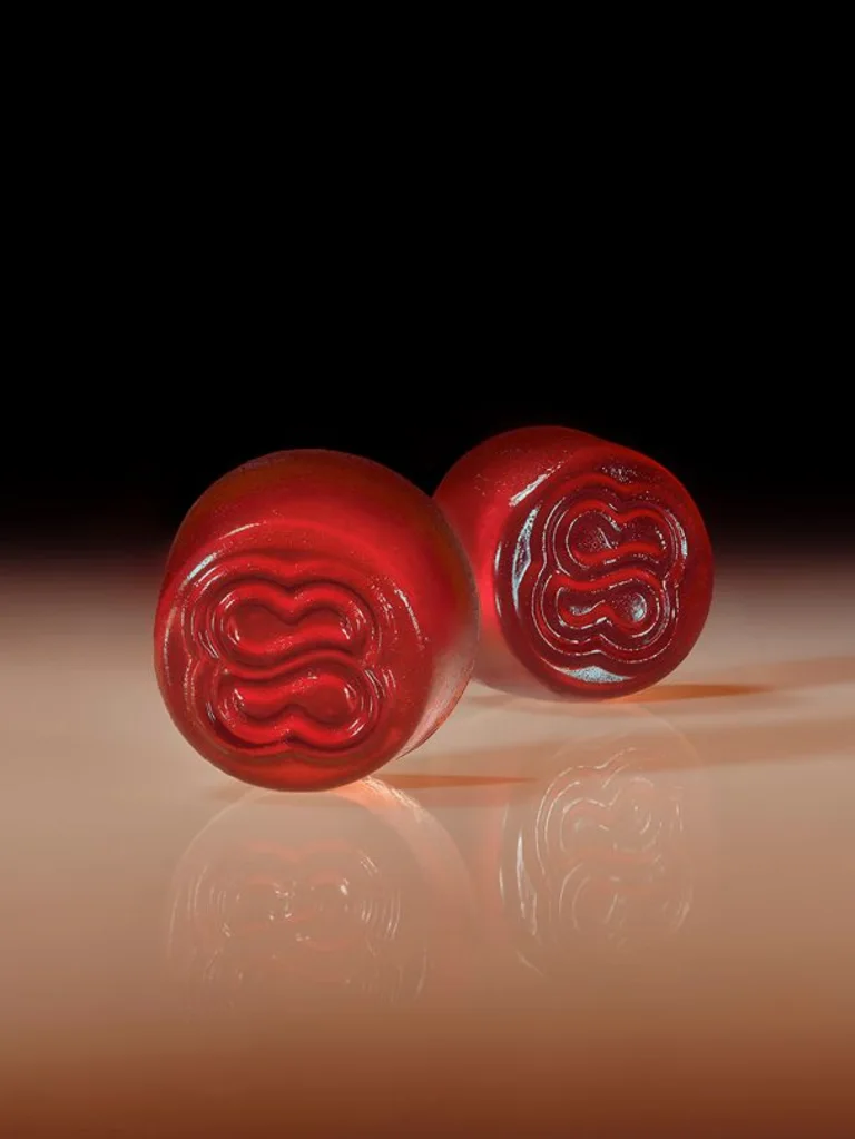 Two translucent red Sakara Serene State stress release gummies with embossed logo on warm brown gradient background with glossy reflective surface