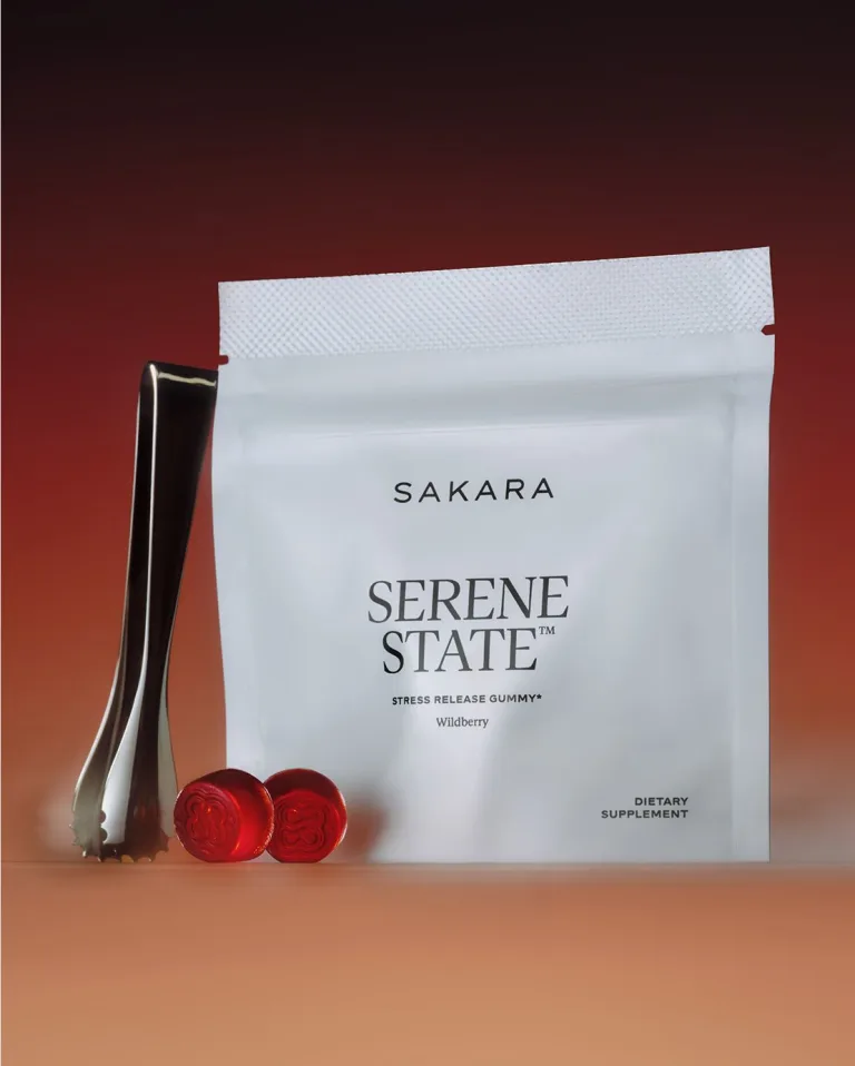Sakara Serene State stress release gummies in matte white pouch with black text, Wildberry flavor, 14 gummies dietary supplement, shown on warm orange gradient background with metal tong and two red gummies in front