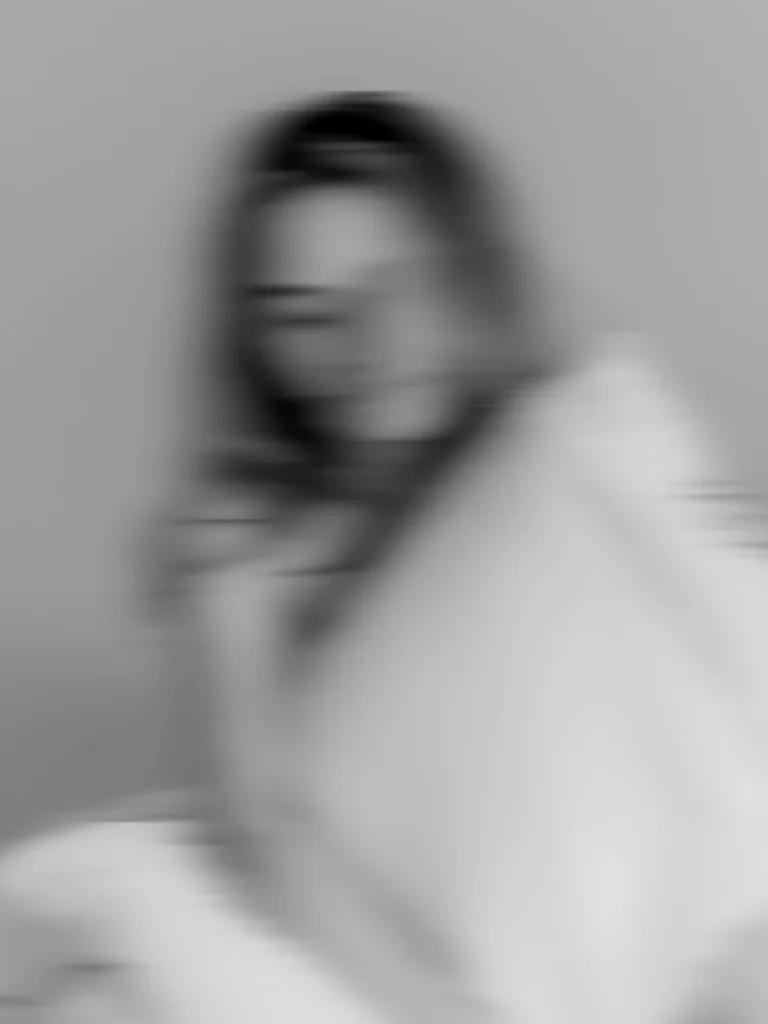 Blurred black-and-white portrait of a woman against a neutral background.