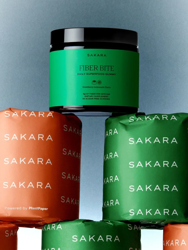 Five packs of Sakara toilet paper in green and tangerine with Sakara Fiber Bite stacked on top